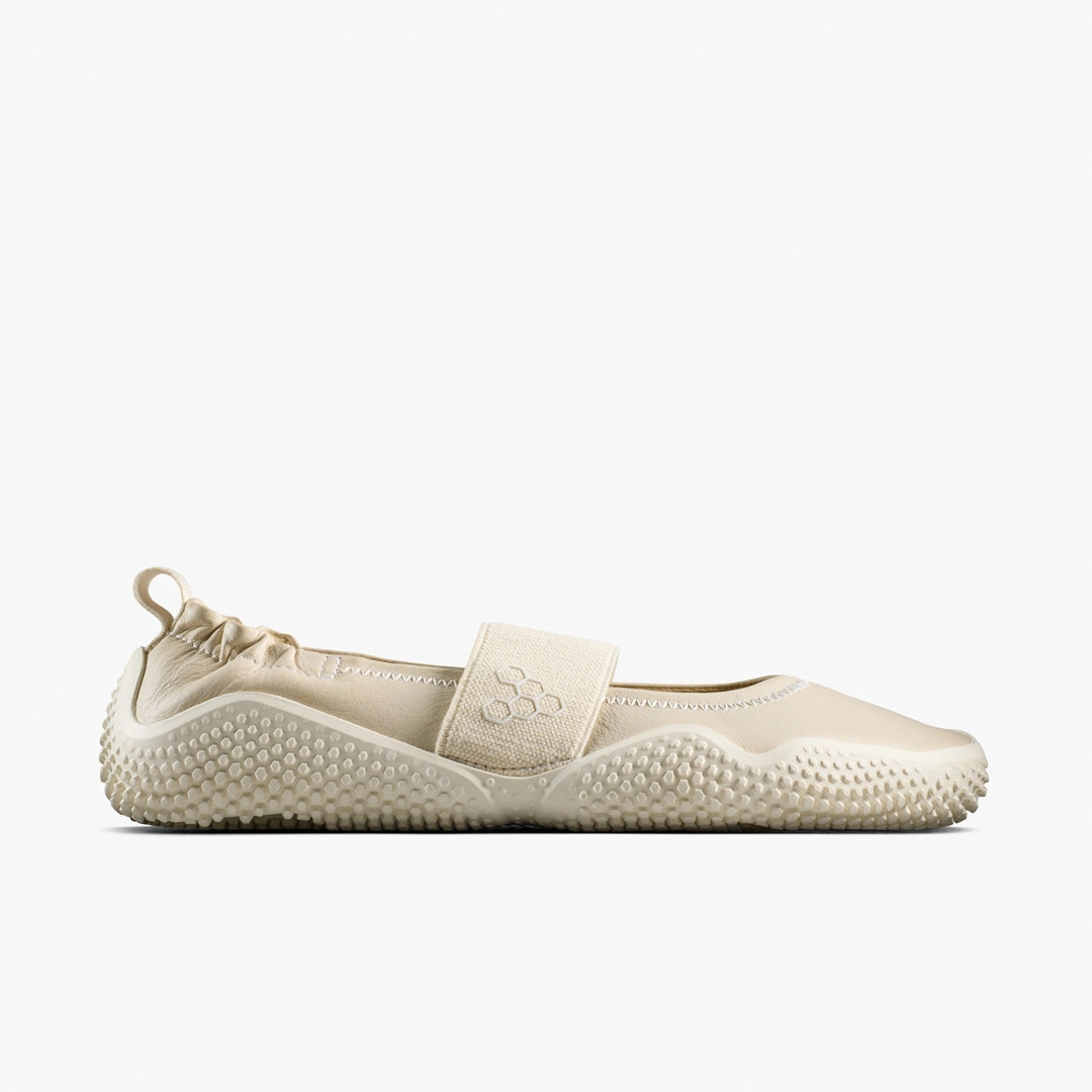The Motus Studio Ballet (Women's) by VIVOBAREFOOT is a beige minimalist shoe with Wild Hide leather, textured sole, elastic heel, Velcro strap with embossed logo, and a low-cut Mary Jane-inspired fit.