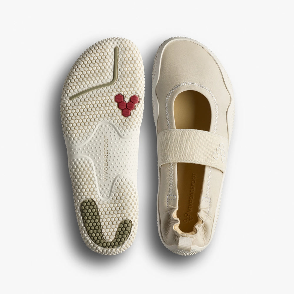 The VIVOBAREFOOT Motus Studio Ballet (Women's) are cream-colored Mary Janes made from Wild Hide leather with an elastic strap, shown top and bottom. The minimalist soles have textured patterns and colored accents.