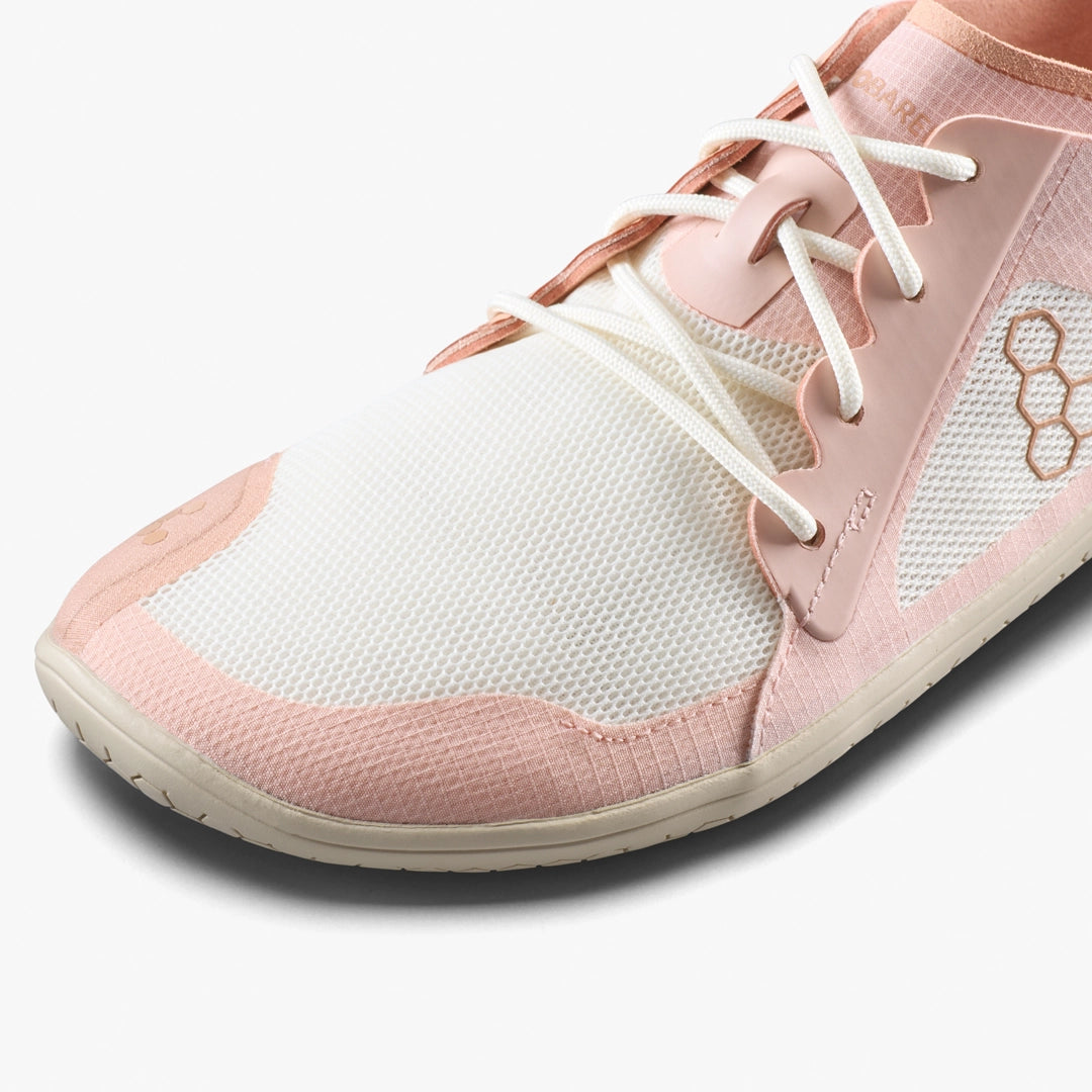 Close-up of the VIVOBAREFOOT Primus Lite IV (Women's), a light pink and white barefoot trainer with white laces, mesh-like upper, hexagon side pattern, and smooth overlays for natural movement.