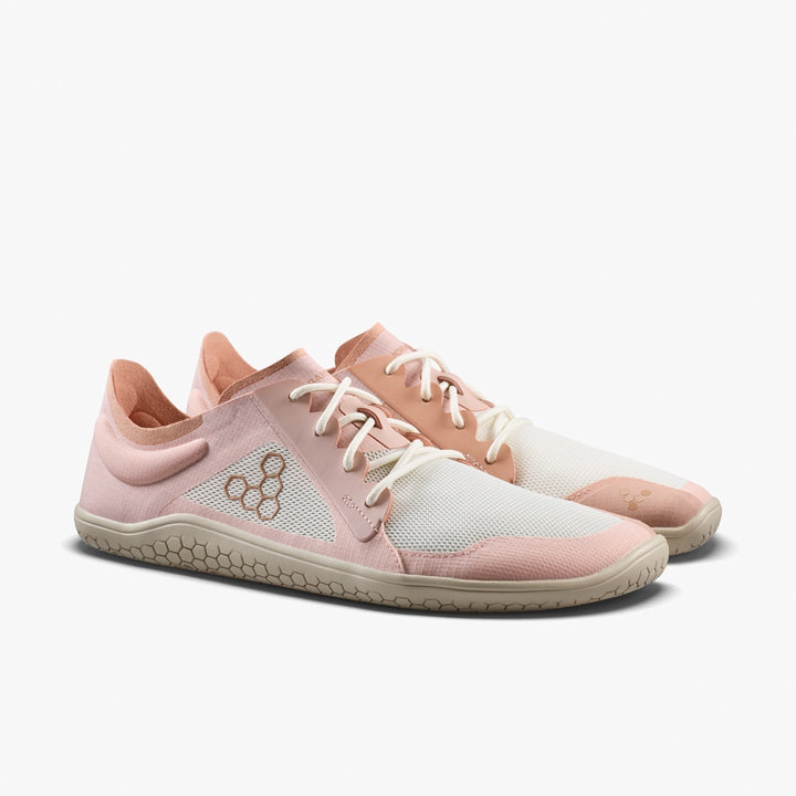 The VIVOBAREFOOT Primus Lite IV (Women's) is a pair of lightweight, low-profile barefoot trainers in white and light pink with beige soles, white laces, a hexagonal logo, and a sleek minimalist design that encourages natural movement.