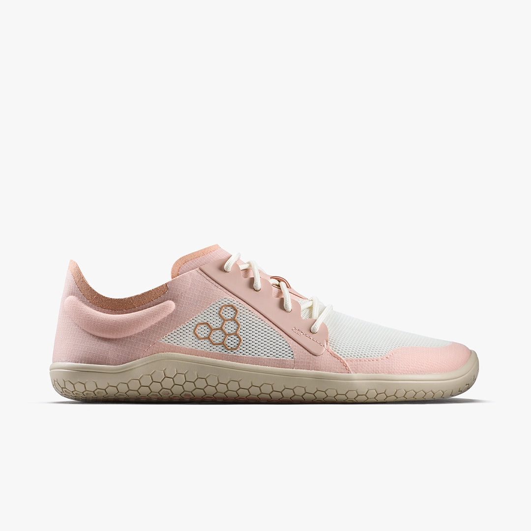 The VIVOBAREFOOT Primus Lite IV (Women's) is a minimalist barefoot trainer with a pink and white mesh upper, white laces, and a beige flexible sole featuring a honeycomb pattern for natural movement.