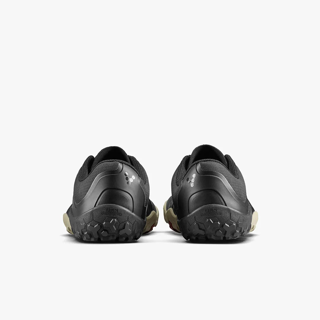 A pair of VIVOBAREFOOT Primus Trail III All Weather FG women's shoes in black, displayed from the back to highlight their textured soles and small reflective logo on each heel, set against a plain white background.