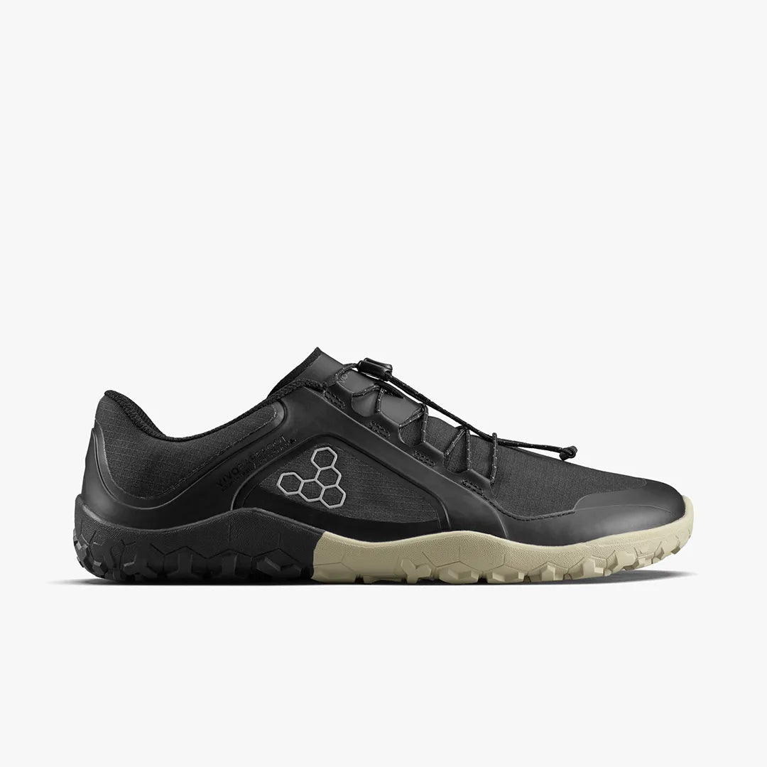Side view of a black VIVOBAREFOOT Primus Trail III All Weather FG (Women's) minimalist trail running shoe with a toggle lacing system. This vegan trail shoe features a technical synthetic upper, structured heel, and a lugged sole that transitions from black at the heel to tan at the toe—combining performance and ethical design for adventurous terrains.