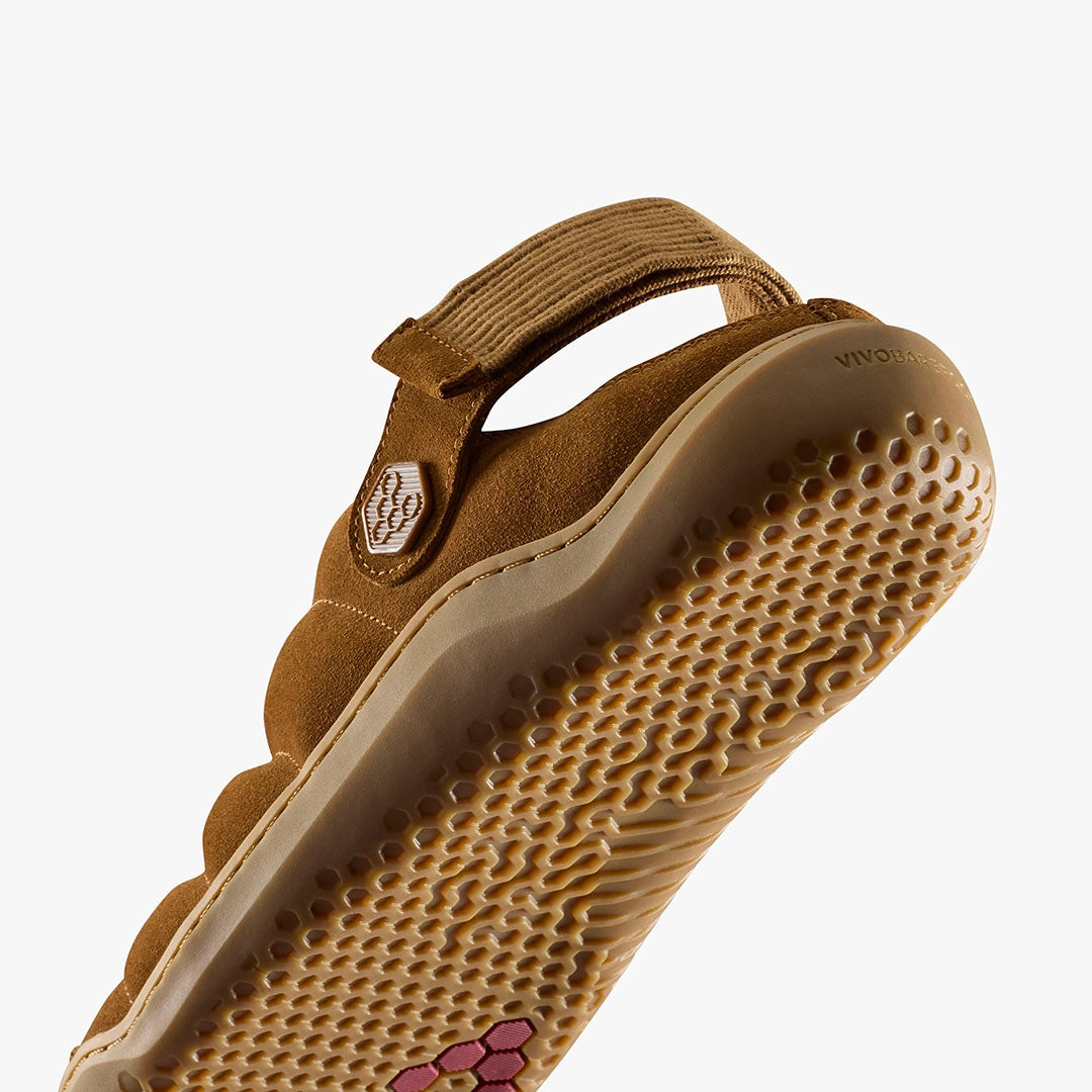 A close-up of the Gobi Wavey Mule (Men's), a tan suede shoe with a textured beige sole, grip patterns, and an adjustable back strap. The VIVOBAREFOOT logo appears near the heel on this cozy cold-weather slipper.
