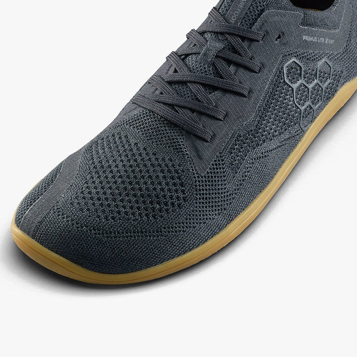A close-up of the STRIDE LAB USA Primus Lite Knit Natural (Women's) shows its dark gray mesh upper, hexagonal side pattern, recycled PU insole, and light brown rubber sole on a white background.