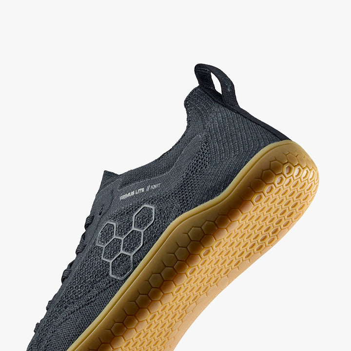 The Primus Lite Knit Natural (Women's) by STRIDE LAB USA is a dark gray barefoot performance trainer with a light brown honeycomb-patterned sole, mesh upper, pull tab at the heel, and minimalist design, shown on a white background.