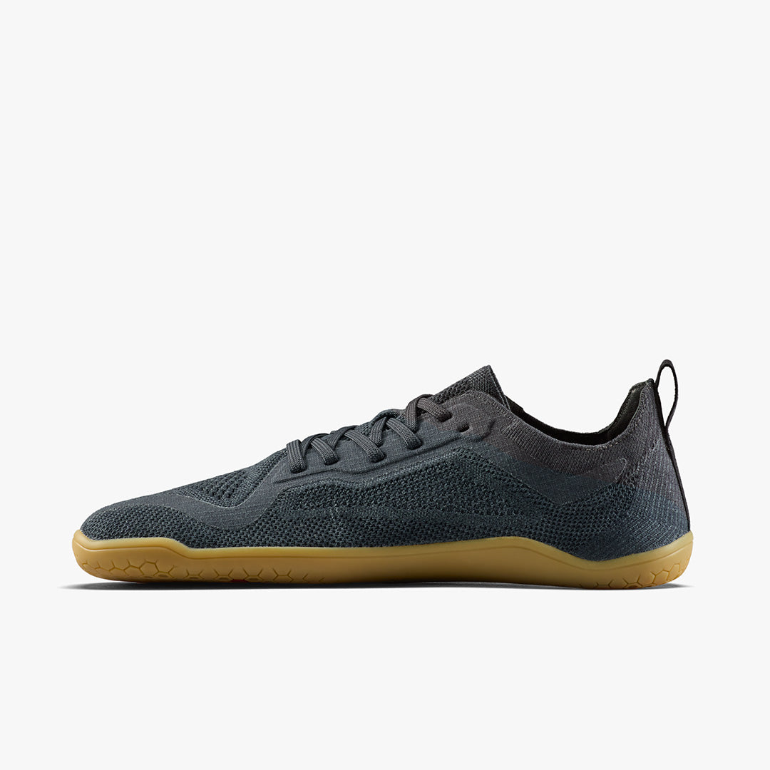 The STRIDE LAB USA Primus Lite Knit Natural (Women's) is a minimalist dark gray barefoot performance trainer with a mesh upper, black heel tab, recycled PU insole, and light brown rubber sole, shown in side profile on a white background.