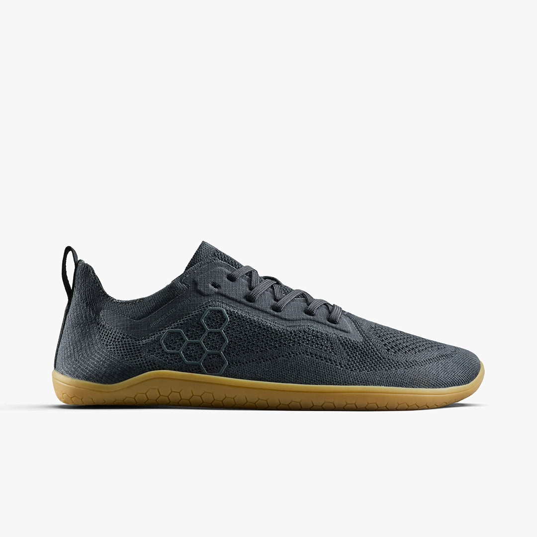 The STRIDE LAB USA Primus Lite Knit Natural (Women's) is a dark gray barefoot performance trainer featuring a low profile, honeycomb side pattern, black laces, light brown rubber sole, and recycled PU insole against a white background.