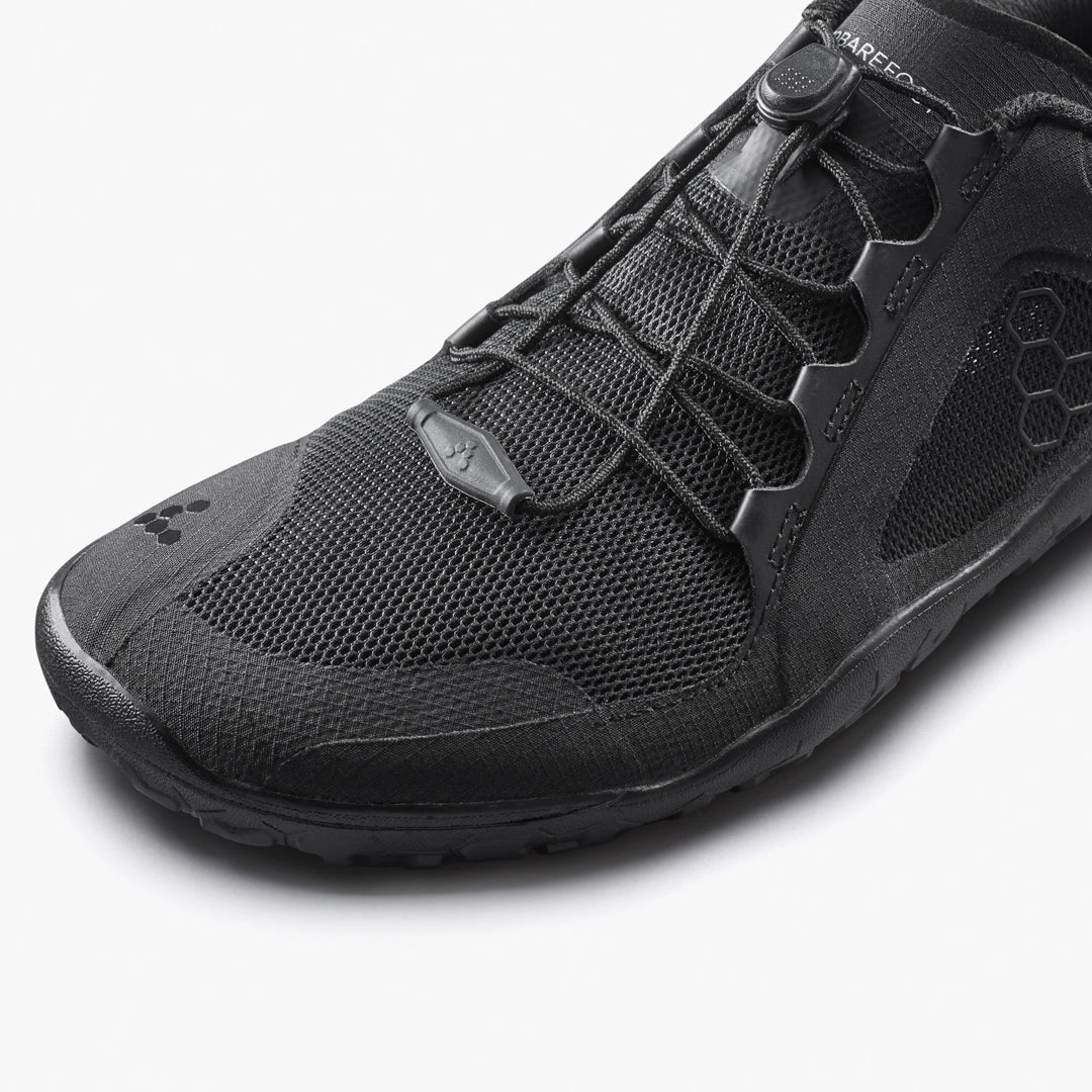 Close-up of the VIVOBAREFOOT Primus Trail 3.5 (Women's) black trail running shoe, featuring a recycled mesh upper, hexagonal pattern details, and elastic toggle laces on a white background.