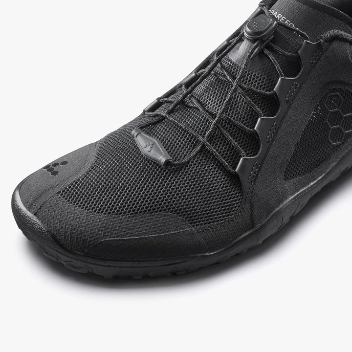 Close-up of the VIVOBAREFOOT Primus Trail 3.5 (Women's) black trail running shoe, featuring a recycled mesh upper, hexagonal pattern details, and elastic toggle laces on a white background.