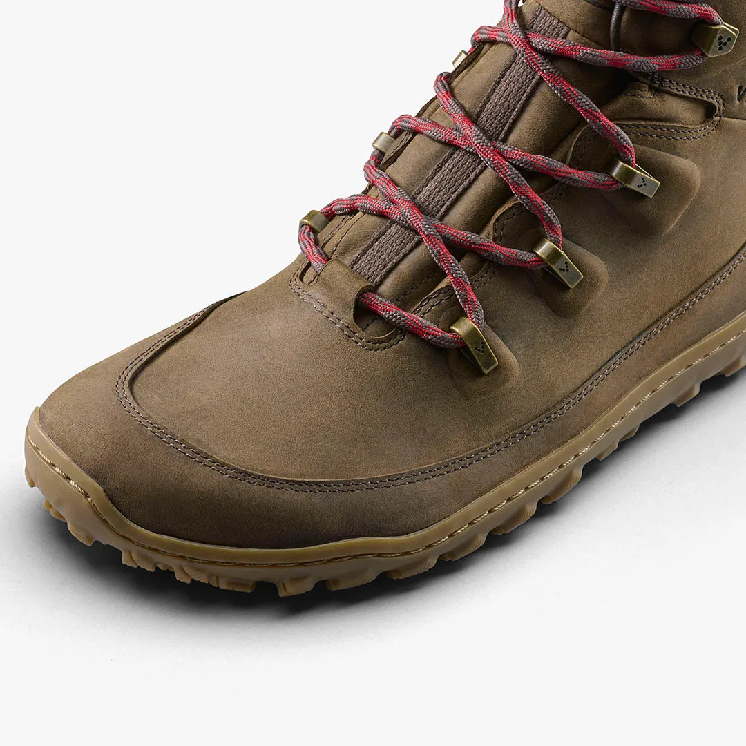 A close-up of the VIVOBAREFOOT Tracker Leather AT II (Women's) hiking boot in brown, featuring red and brown laces, metal eyelets, and a rugged tread for all-terrain use, shown against a white background.