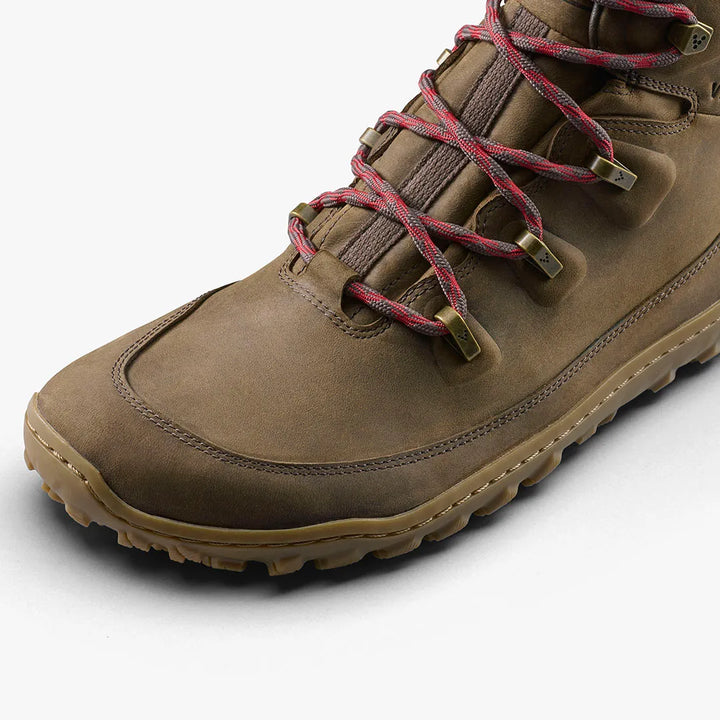 A close-up of the VIVOBAREFOOT Tracker Leather AT II (Men's) hiking boot in brown, featuring red and brown laces, metal eyelets, and a rugged rubber sole for all-terrain performance, shown on a white background.