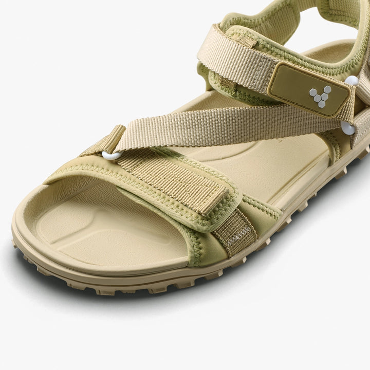 Close-up of the VIVOBAREFOOT Tracker Ora Sandal (Men's) in beige, featuring adjustable Velcro straps, a neoprene upper, rugged sole for outdoor comfort, and a small geometric logo near the ankle strap.