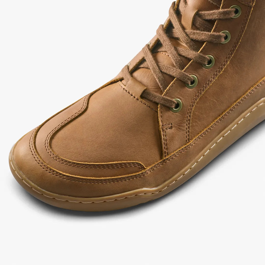 Close-up of a brown leather VIVOBAREFOOT Gobi Boot II Warmlined (Men’s), a warm-lined lace-up ankle boot with a rounded toe and a thin, flat sole.