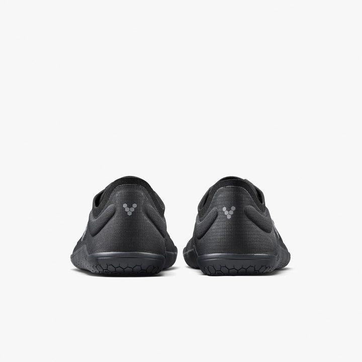 A pair of black VIVOBAREFOOT Primus Lite IV men's minimalist performance trainers, shown from the back on a plain white background, featuring textured soles and a small hexagonal logo on each heel.