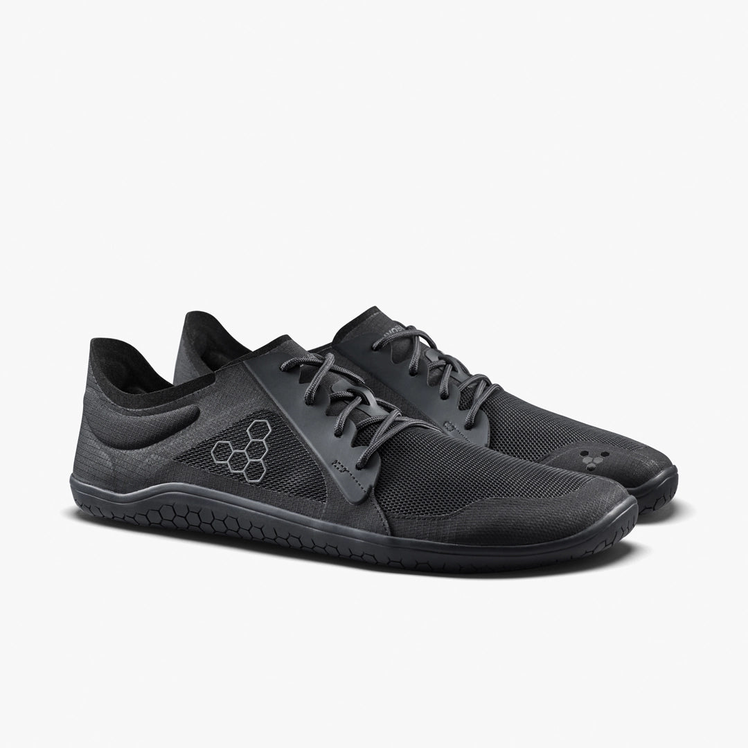 The VIVOBAREFOOT Primus Lite IV (Men's) is a black minimalist performance trainer with mesh uppers, lace-up closure, thin flexible soles, and a hexagonal logo on the side, shown against a plain white background.