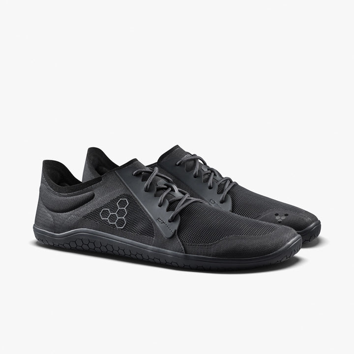 The VIVOBAREFOOT Primus Lite IV (Men's) is a black minimalist performance trainer with mesh uppers, lace-up closure, thin flexible soles, and a hexagonal logo on the side, shown against a plain white background.
