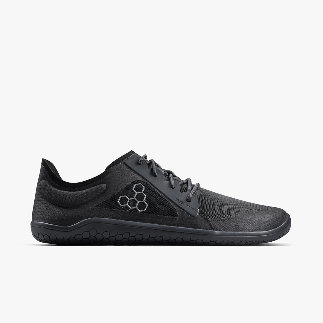 The VIVOBAREFOOT Primus Lite IV (Men's) is a black, minimalist performance trainer with a low-profile lace-up design, recycled mesh upper, and hexagonal side logo, shown in left side view against a plain white background.