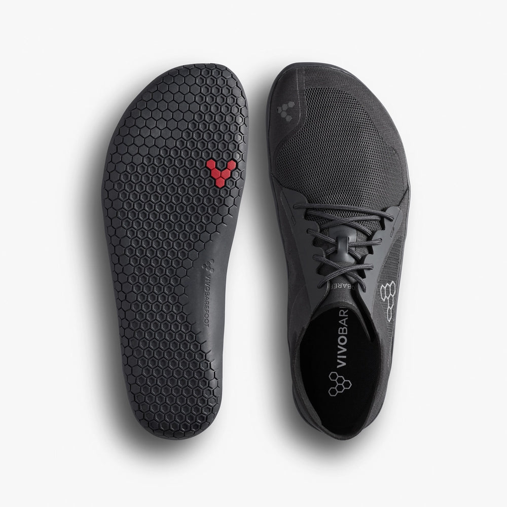 The VIVOBAREFOOT Primus Lite IV (Men's) is a black minimalist barefoot running shoe with a hexagonal-patterned sole featuring red honeycomb detail and a lace-up upper with the logo. Made from recycled materials for eco-conscious performance.