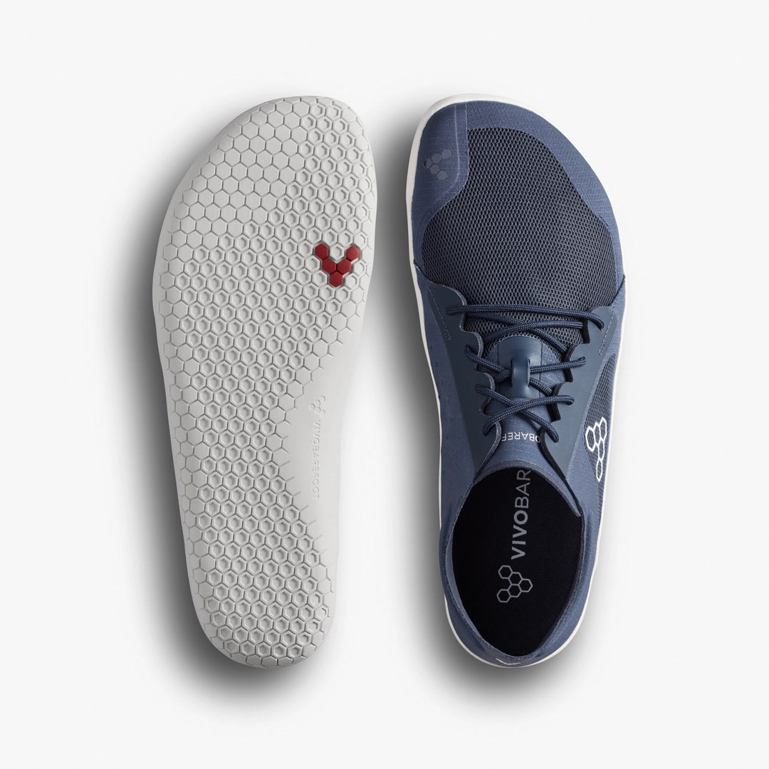 Top and bottom view of the VIVOBAREFOOT Primus Lite IV (Men’s), a minimalist blue barefoot trainer with a white hexagonal-patterned sole, red hexagon detail near the toe, and branding. Designed to promote natural movement.