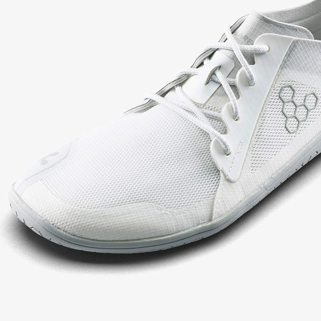 A close-up of the VIVOBAREFOOT Primus Lite IV (Men's), a white performance trainer featuring a minimalist mesh upper, hexagonal logo on the side, white laces, and a thin flexible sole inspired by barefoot running.