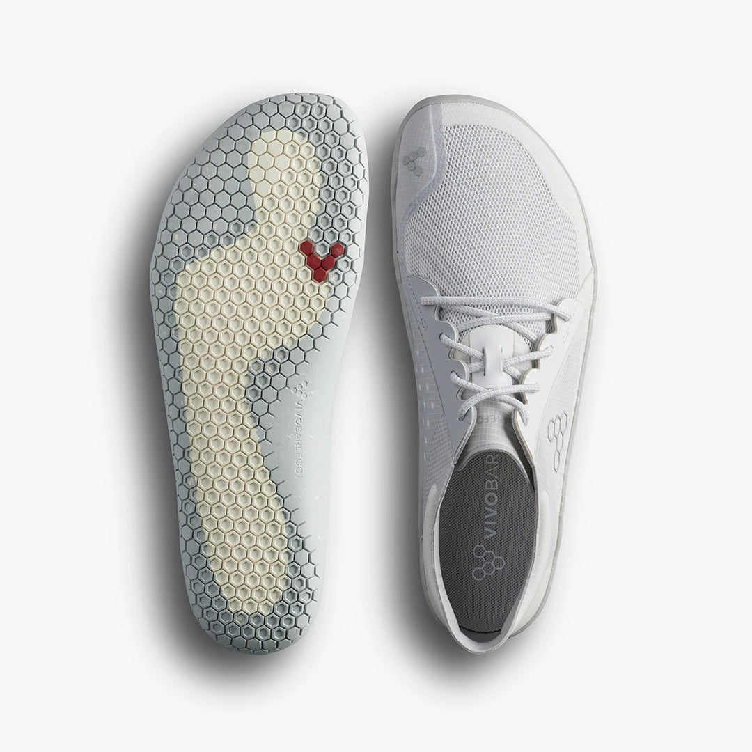 The Primus Lite IV (Men's) by VIVOBAREFOOT is a pair of minimalist white barefoot running shoes with a honeycomb-patterned sole, red hexagon toe detail, recycled materials, gray insole, and VIVOBAREFOOT branding.