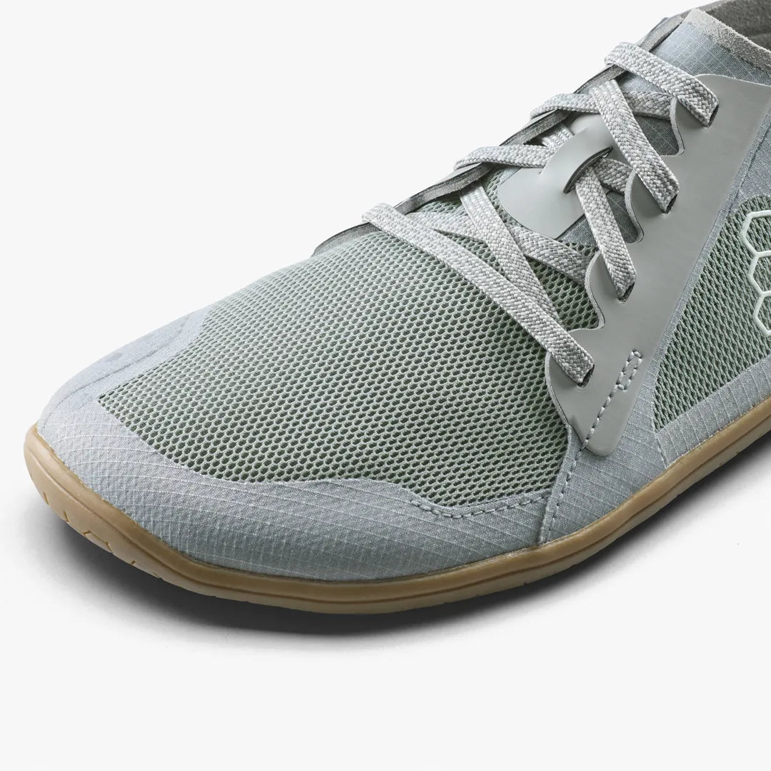 A close-up of a grey mesh VIVOBAREFOOT Primus Lite IV (Men’s) minimalist vegan running shoe with a flat gum sole.