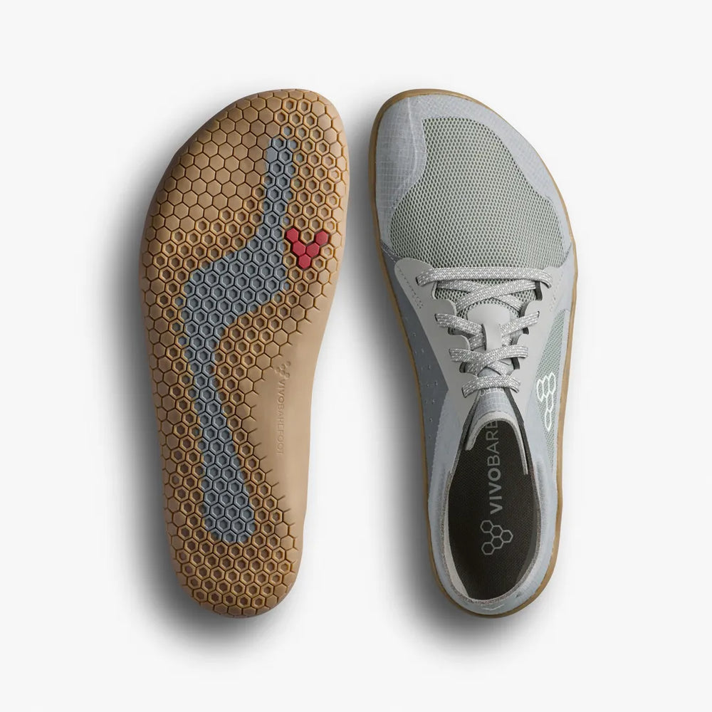 A pair of VIVOBAREFOOT Primus Lite IV (Men’s) barefoot training shoes shown from above, displaying the gray mesh upper of one and the textured hexagonal-patterned rubber sole of the other.