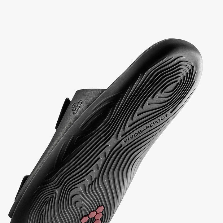 Close-up of the black sole on the VIVOBAREFOOT Sensus Yin Slide (Men’s), showing textured tread patterns with Earthfoam technology and the VIVOBAREFOOT logo, all set against a white background.