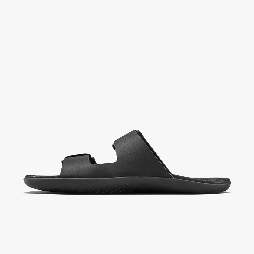 The VIVOBAREFOOT Sensus Yin Slide (Men’s) is a black sandal with two wide chrome-free Taro leather straps and a contoured Earthfoam footbed, shown in profile against a plain white background.