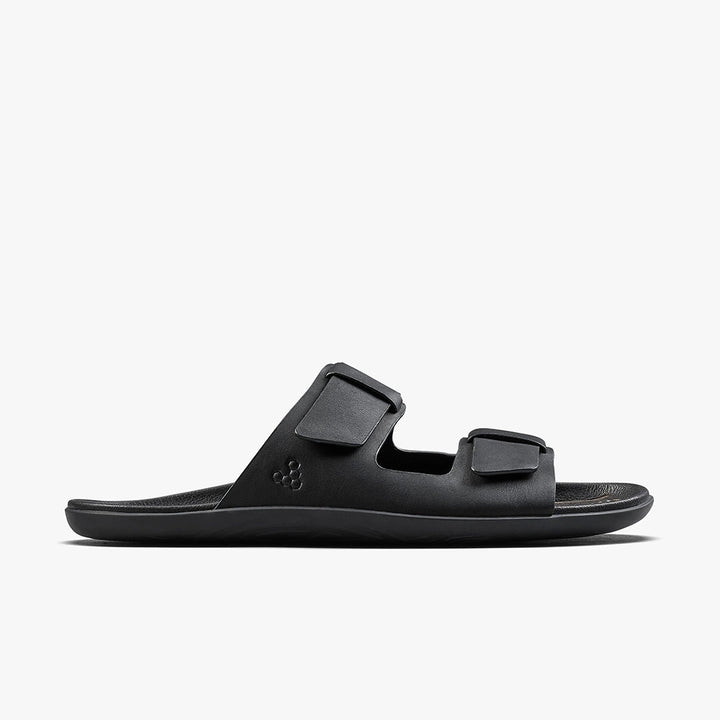The VIVOBAREFOOT Sensus Yin Slide (Men’s) is a black sandal with two adjustable straps and a textured footbed, crafted from chrome-free Taro leather and shown in side profile on a plain white background.
