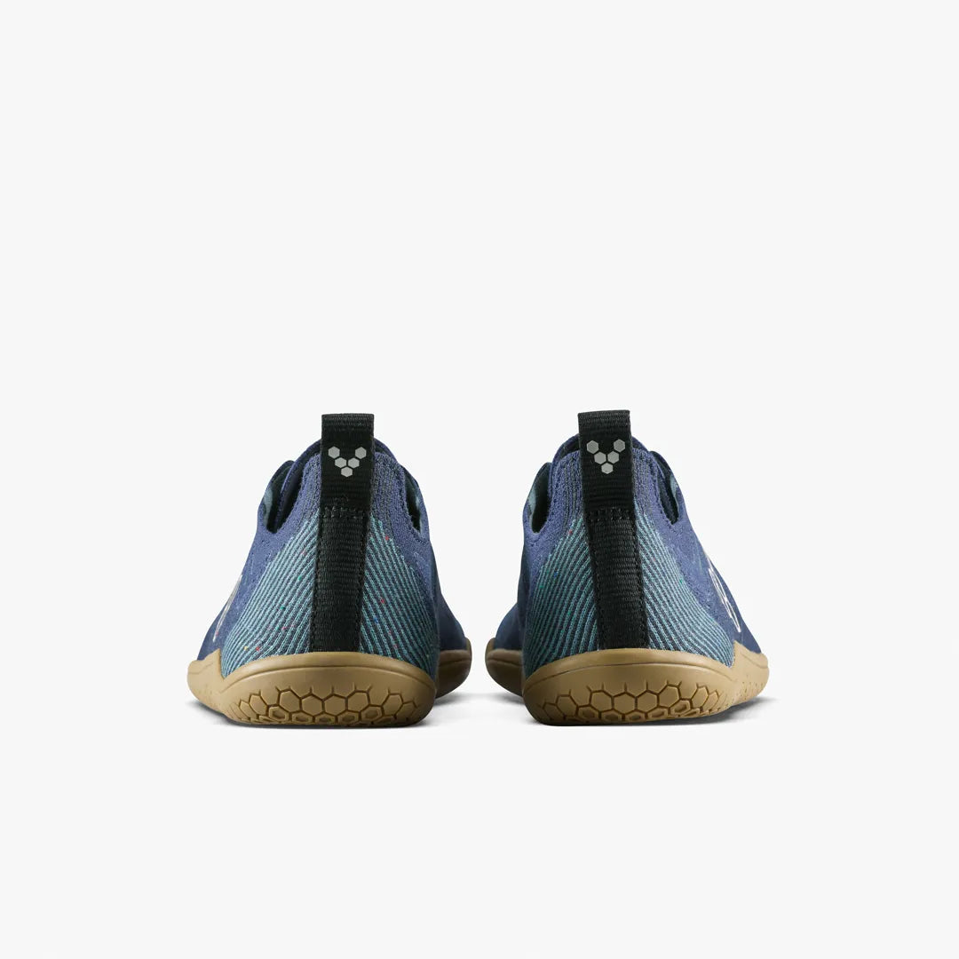 A pair of Primus Lite Knit Natural (Men’s) barefoot performance trainers by VIVOBAREFOOT is shown from the back against a white background, featuring blue knitted uppers, tan soles, black heel loops with a small white logo on the heel tabs.