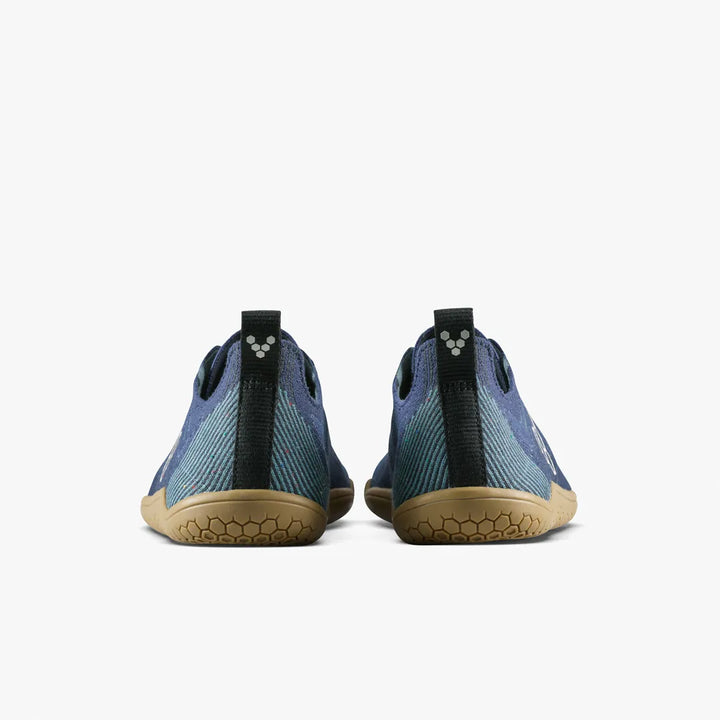 A pair of Primus Lite Knit Natural (Men’s) barefoot performance trainers by VIVOBAREFOOT is shown from the back against a white background, featuring blue knitted uppers, tan soles, black heel loops with a small white logo on the heel tabs.