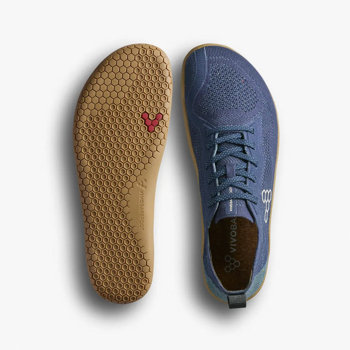 A pair of blue VIVOBAREFOOT Primus Lite Knit Natural (Men’s) shoes, designed as natural workout footwear, with one shoe shown from the top and the other from the bottom, highlighting a honeycomb-patterned sole featuring a small red hexagon detail.
