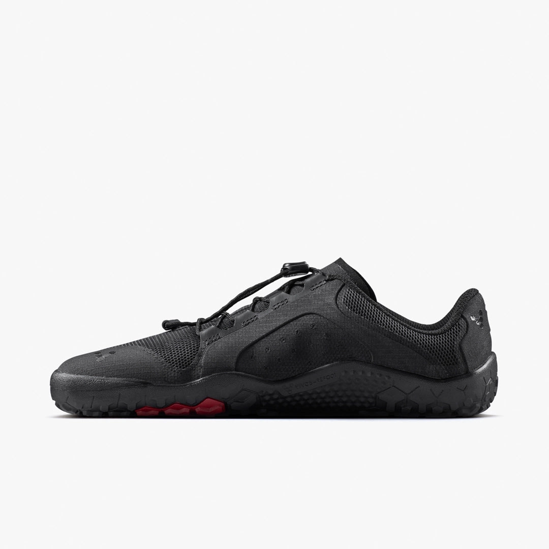 The VIVOBAREFOOT Primus Trail FG 3.5 (Men's) is a black, low-profile all-terrain trainer with a breathable mesh upper, rugged sole with red toe accents, and lace toggle, shown from the side on a plain white background.
