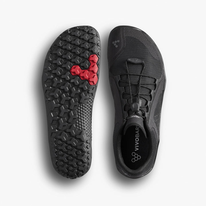 Top view of the VIVOBAREFOOT Primus Trail FG 3.5 (Men's) in black next to its sole, showing breathable mesh, a hexagonal tread with a red cluster at the forefoot, lace toggle, and VIVOBAREFOOT branding on the insole.