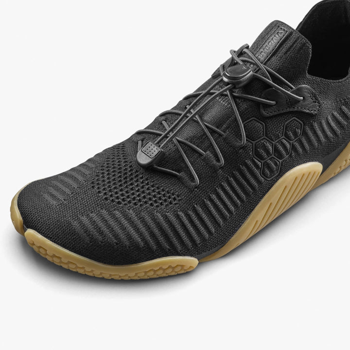 The VIVOBAREFOOT Motus Flex Natural (Men's) is a black athletic shoe with a knit upper, honeycomb pattern, elastic toggle laces, and a textured tan natural rubber outsole—ideal for comfort and grip during calisthenics.