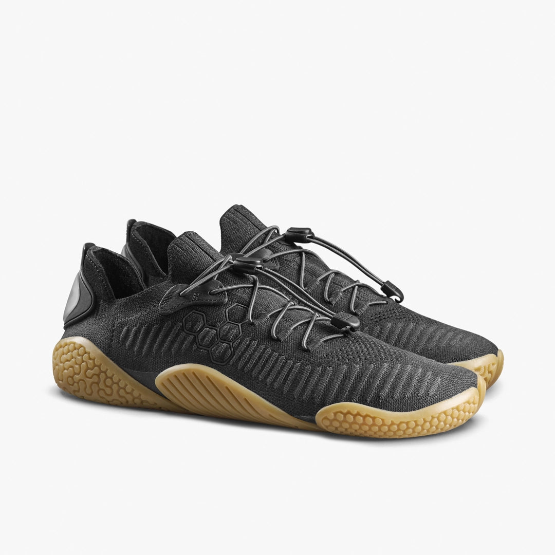 The VIVOBAREFOOT Motus Flex Natural (Women's) are black athletic sneakers with textured light brown natural rubber soles and a unique lacing system, ideal for bodyweight training, shown on a white background.