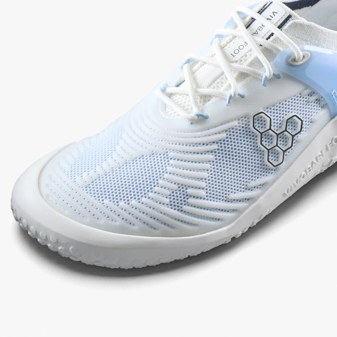 Close-up of the VIVOBAREFOOT Motus Strength II (Men's): a white barefoot trainer with light blue accents, textured upper, hexagonal side pattern, white laces, and visible branding; perfect for CrossFit or high-impact workouts. Partial sole is also shown.