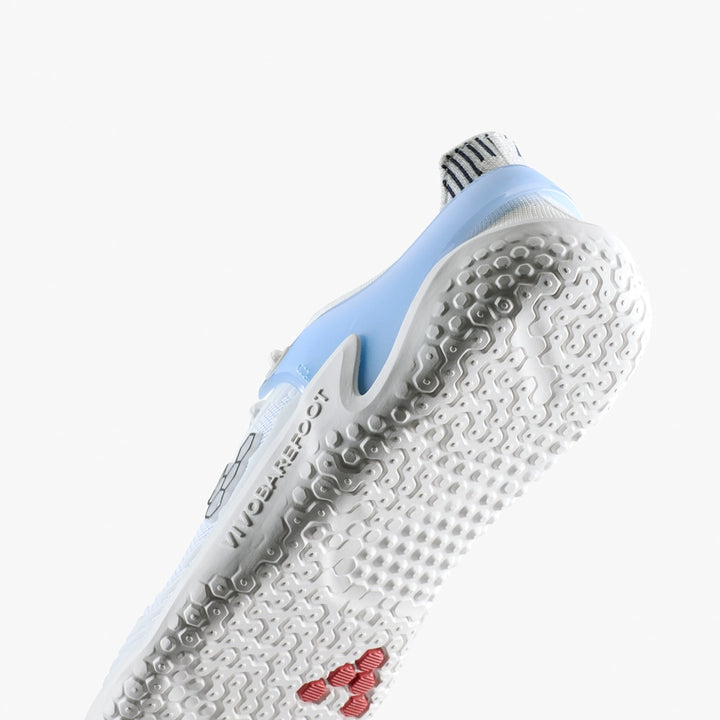 A close-up of the white sole on the VIVOBAREFOOT Motus Strength II (Men's) in light blue, showing textured grip for intense workouts, "NO BAREFOOT" embossed on the side, a striped heel design, and a small red logo by the toe.