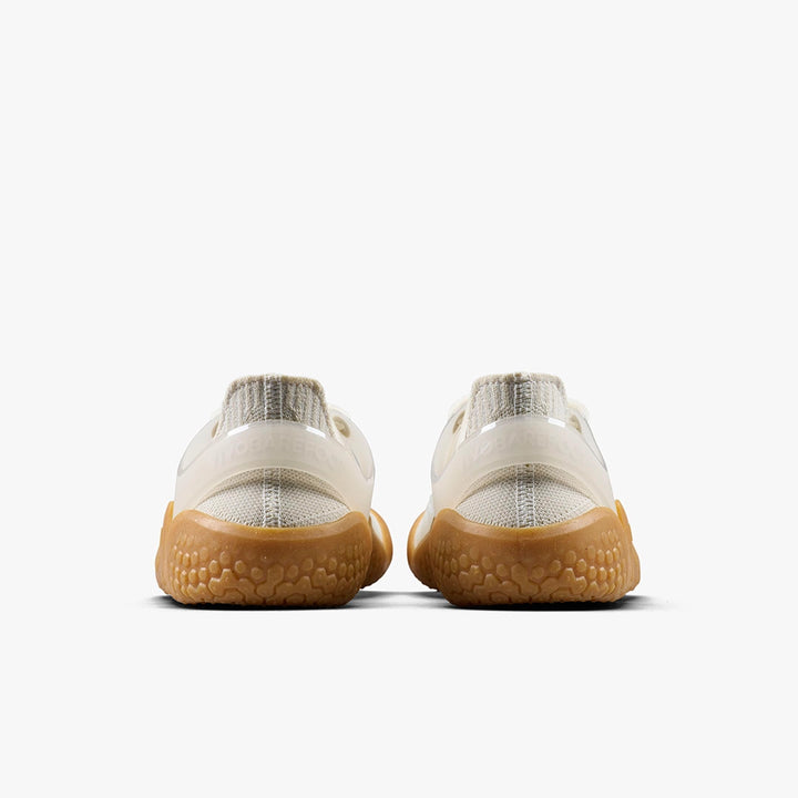 The Motus Strength II (Men's) by VIVOBAREFOOT are beige and white barefoot trainers with textured light brown soles for enhanced grip and stability, shown from the back on a plain white background.