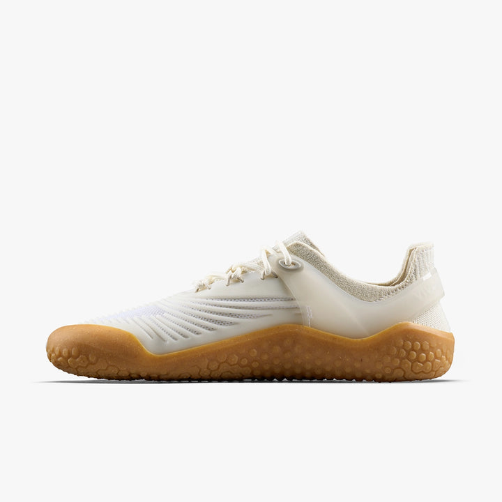 The VIVOBAREFOOT Motus Strength II (Women’s) is a minimalist barefoot trainer with a white upper, textured accents, and a thick honey-colored gum sole. Shown in side profile on white. Ideal for functional fitness and high-impact workouts.