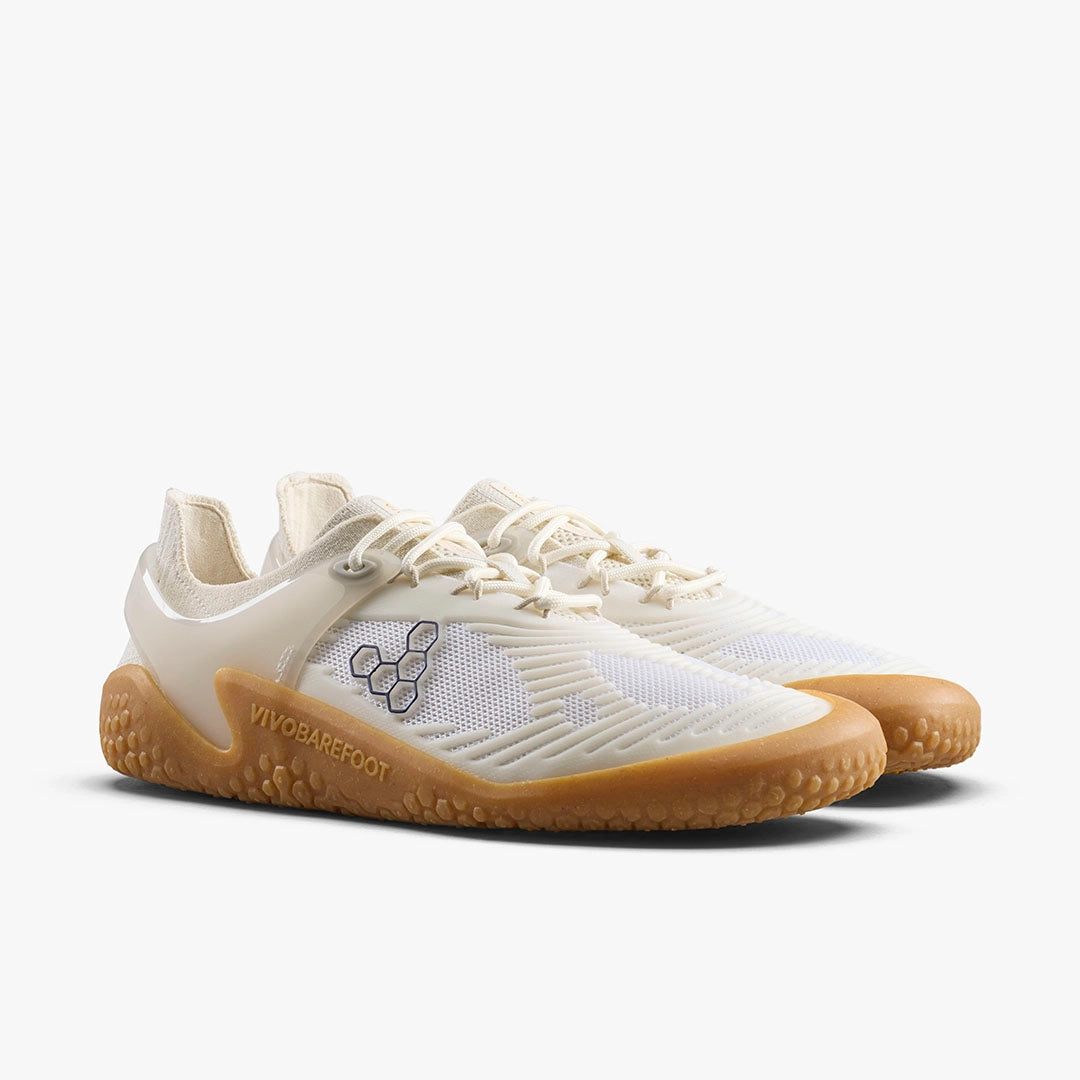 The VIVOBAREFOOT Motus Strength II (Women's) trainers feature off-white and beige mesh uppers, gum soles, and side logos—ideal barefoot shoes for functional fitness, shown on a white background.