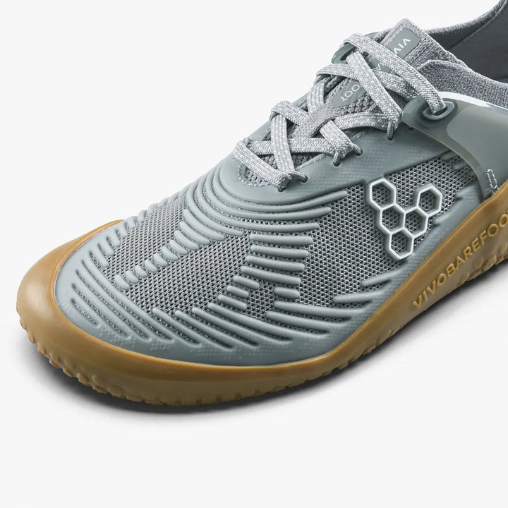 Close-up of a grey VIVOBAREFOOT Motus Strength II (Men’s) barefoot strength trainer with a gum-colored sole, breathable mesh upper, and a hexagonal logo on the side.