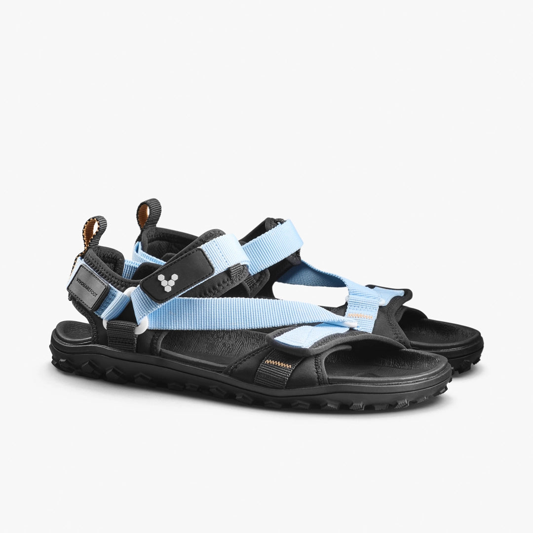The VIVOBAREFOOT Tracker Ora Sandal (Men's) features black all-terrain soles, light blue adjustable straps, a white side logo, and open toes and heels—ideal barefoot sandals for outdoor or casual wear.