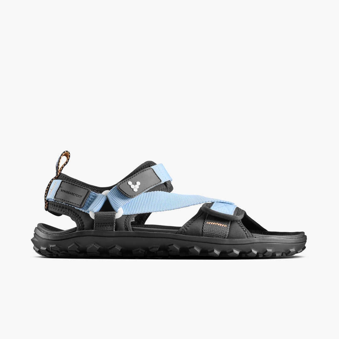 The VIVOBAREFOOT Tracker Ora Sandal (Men's) features a black minimalist design with light blue adjustable straps, rugged sole, neoprene upper, and a heel strap with loop—perfect for all-terrain use. Displayed on a plain white background.