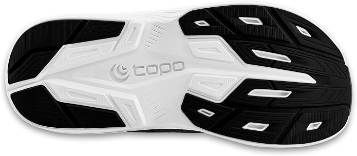 The image shows the black and white rubber outsole of the Magnifly 6 (Women’s) by TOPO, one of the brand’s zero drop running shoes. The outsole features grooves and geometric tread patterns for traction, delivering a stable foundation beneath these cushioned running shoes. The word “TOPO” is embossed in the center.
