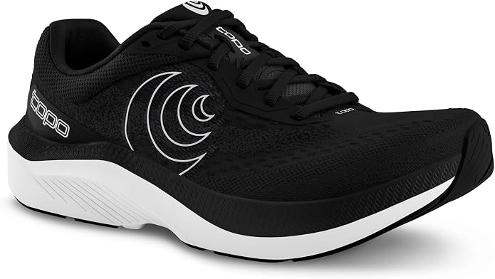 Introducing the TOPO Magnifly 6 (Women’s): a black athletic running shoe with stylish white accents and a distinctive wave-like design along the side. Built on a thick, cushioned white sole, this shoe delivers exceptional comfort and reliable support for every stride. Featuring black laces and a branded logo near the tongue, the Magnifly 6 (Women’s) combines function and fashion—perfect for runners seeking performance inspired by classic cushioned footwear.