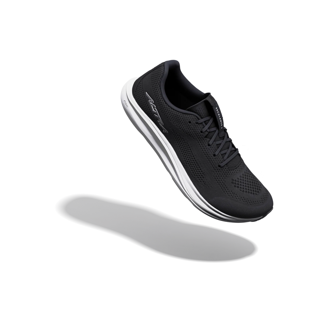 A black ALTRA Escalante 5 (Men’s) running shoe with white accents is displayed suspended mid-air above a subtle shadow against a plain white background, highlighting its distinctive FootShape™ Fit and zero drop design.