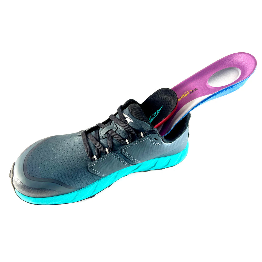 A pair of Bridge Soles athletic shoes in gray and teal, featuring a partially inserted purple Bridge Soles orthopedic insole, is displayed on a white background.